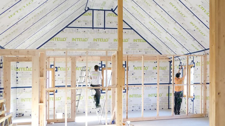 Two tradespeople installing INTELLO membranes inside the roof and walls of a bright house.